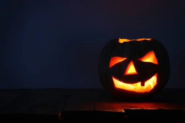Calabaza de Halloween en la mesa de madera frente al espeluznante fondo oscuro. Jack o linterna — Foto de Stock