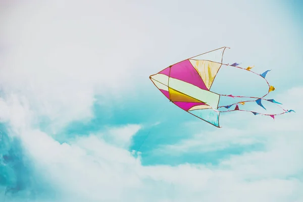 Pipa colorida voando no céu azul através das nuvens — Fotografia de Stock