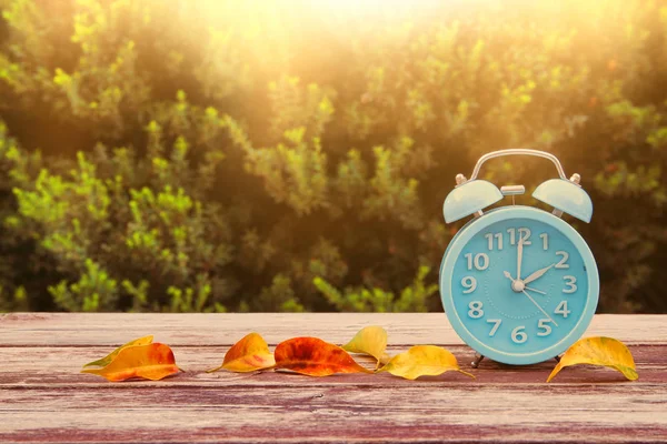 Imagen de otoño Cambio de Tiempo. Concepto de retroceso. Hojas secas y alarma vintage Reloj en mesa de madera al aire libre por la tarde —  Fotos de Stock