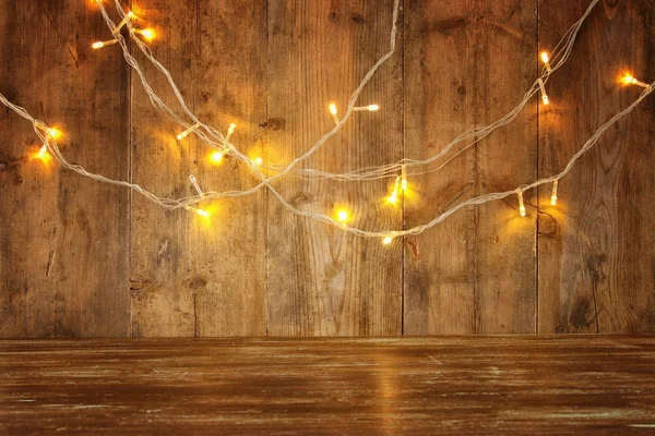 Wood board table in front of Christmas warm gold garland lights on wooden rustic background. glitter overlay — Stock Photo, Image