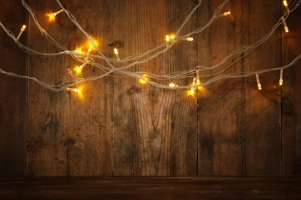 Mesa de madera frente a luces de guirnalda de oro caliente de Navidad sobre fondo rústico de madera. recubrimiento de purpurina — Foto de Stock