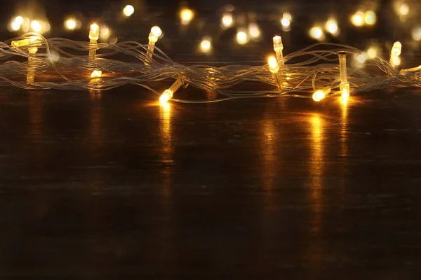 Boże Narodzenie ciepły złoty wianek światła balck drewniane tła. Brokat nakładki. — Zdjęcie stockowe