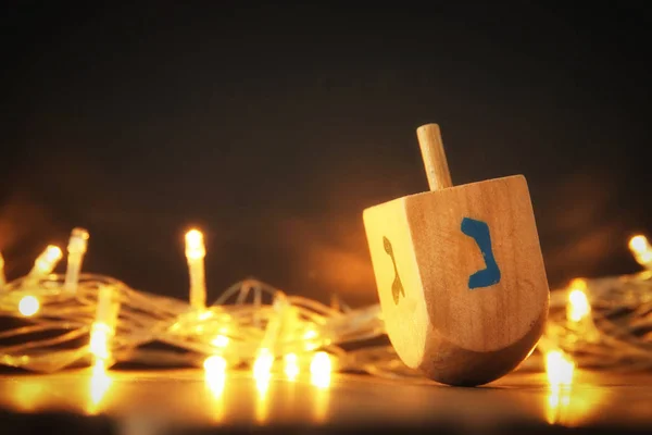 jewish holiday Hanukkah with wooden dreidel (spinning top) and gold lights on the table