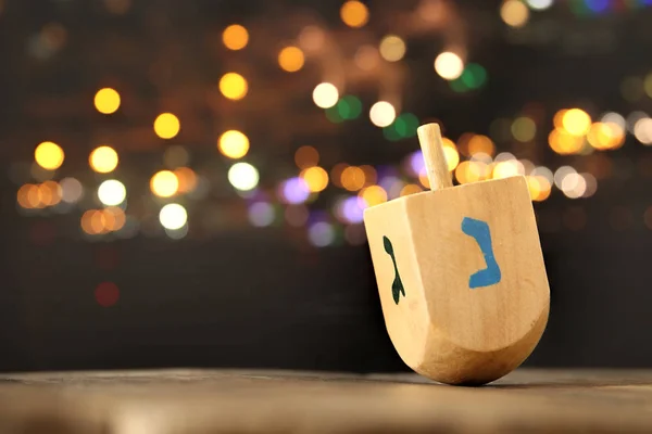 Jewish holiday Hanukkah with wooden dreidel (spinning top) and gold lights on the table — Stock Photo, Image