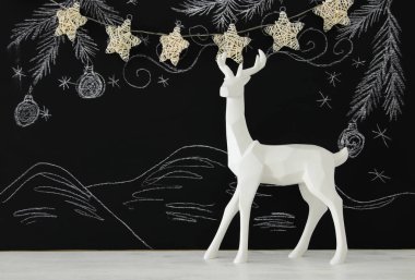 Kara tahta arka plan whith el üzerinde ahşap masa üzerinde beyaz Ren geyiği tebeşir illüstrasyonlar çizilmiş.