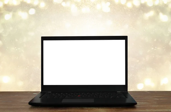 Open laptop with white screen on wooden table in front of abstract glitter background — Stock Photo, Image