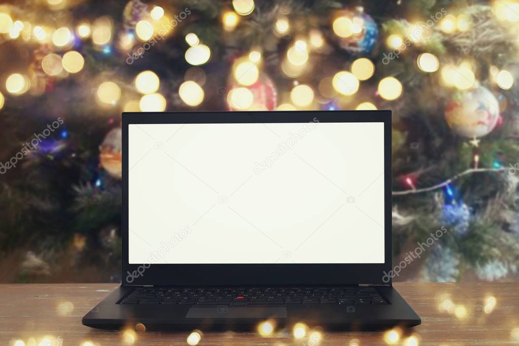 Image of open laptop with white screen on wooden table in front of christmas tree background