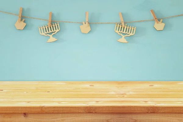 Empty wooden table in front of jewish holiday Hanukkah background with decorative wooden menorah and spinning tops hanging on a rope — Stock Photo, Image