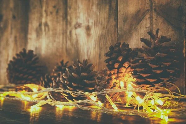 Imagen navideña con luces de guirnalda dorada y conos de pino sobre fondo de madera —  Fotos de Stock