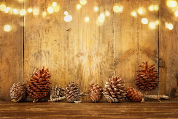 Imagen navideña con luces de guirnalda dorada y conos de pino sobre fondo de madera — Foto de Stock