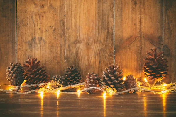 Imagem de férias com luzes douradas da grinalda do Natal e cones de pinho sobre fundo de madeira — Fotografia de Stock