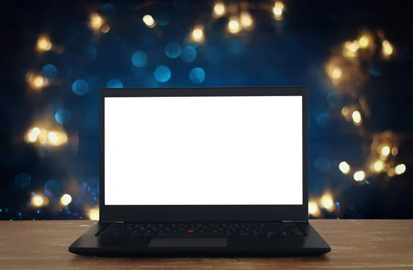 Offener Laptop mit weißem Bildschirm auf Holztisch vor abstraktem Glitzerhintergrund — Stockfoto