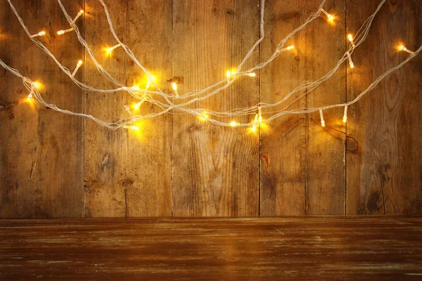 Table en bois devant les lumières chaudes guirlande d'or de Noël sur fond rustique en bois. superposition de paillettes — Photo