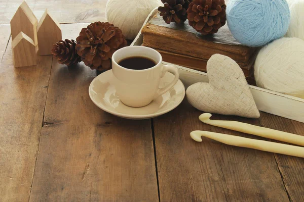 Ciepłe i przytulne przędzy kulki wełny i filiżankę gorącej kawy na drewnianym stole. — Zdjęcie stockowe