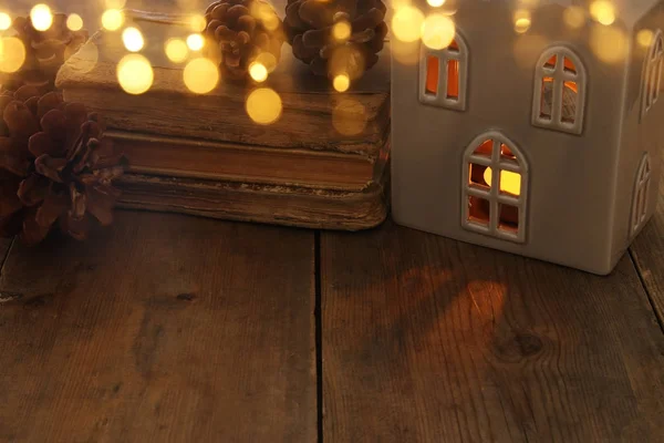 Low key image of house lantern with burning candle and warm light in the windows over old wooden background.