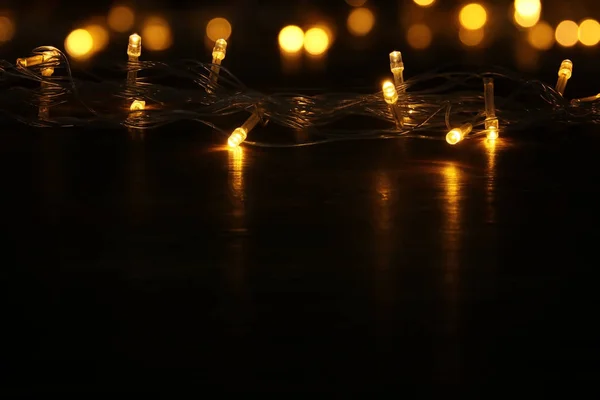 クリスマス温かみのあるゴールドのガーランド ライト balck 木製の背景。キラキラ オーバーレイ. — ストック写真