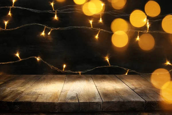 Wood board table in front of Christmas warm gold garland lights on wooden rustic background. — Stock Photo, Image