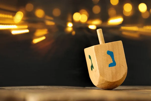 Jüdischer Feiertag Chanukka mit hölzernem Dreidel (Kreisel) und goldenen Lichtern auf dem Tisch — Stockfoto