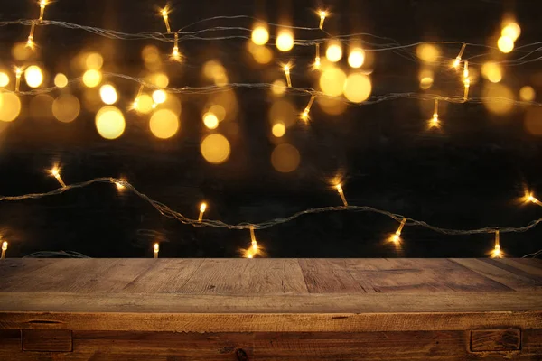 Hout bord tafel in de voorkant van Kerstmis warm goud slinger lichten op houten rustieke achtergrond. — Stockfoto