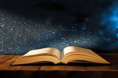 Tahta masanın üzerinde parıltılı kaplamalı açık antik kitap görüntüsü.