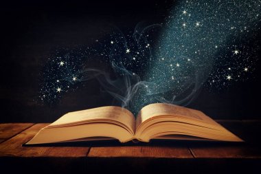 Tahta masanın üzerinde parıltılı kaplamalı açık antik kitap görüntüsü.