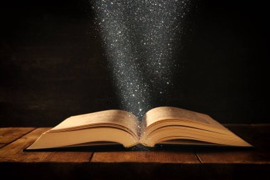 Tahta masanın üzerinde parıltılı kaplamalı açık antik kitap görüntüsü.