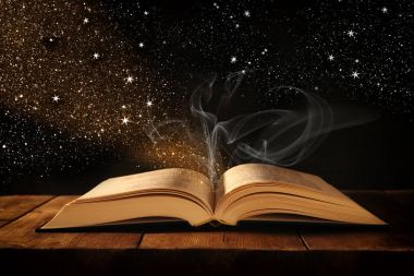 Tahta masanın üzerinde parıltılı kaplamalı açık antik kitap görüntüsü.