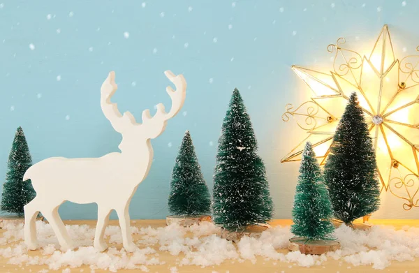 Imagen de árboles de Navidad y renos sobre una mesa de madera nevada —  Fotos de Stock