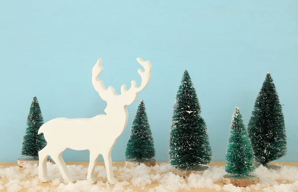 A karácsonyfák és a rénszarvas, a havas fából készült asztal képe — Stock Fotó