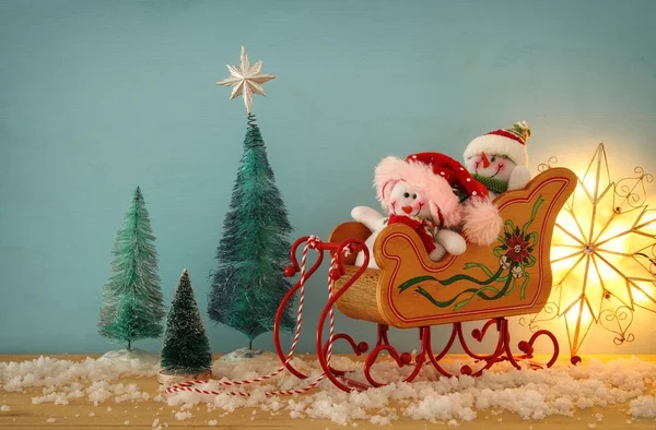 Imagen del árbol de Navidad y muñecos de nieve en el trineo viejo de madera sobre la mesa de madera nevada . —  Fotos de Stock