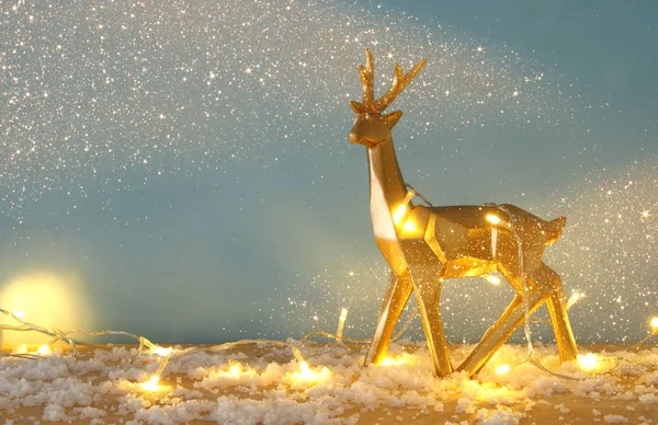 ゴールドの光沢のあるトナカイ クリスマス ガーランド ライトと雪に覆われた木製テーブルの上. — ストック写真