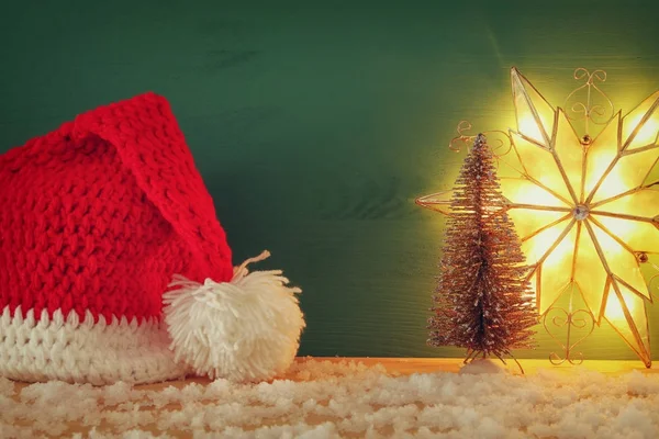 Image des arbres de Noël et du santa claus chapeau sur la table en bois enneigé . — Photo