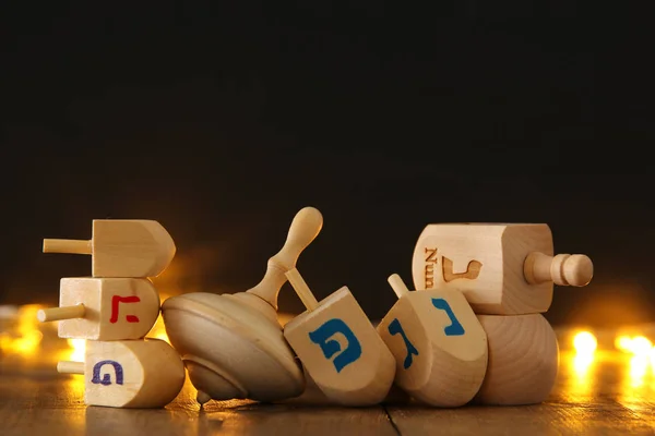 Joodse vakantie Hanukkah met houten dreidels collectie (spinnen boven) en gouden garland licht op tafel — Stockfoto