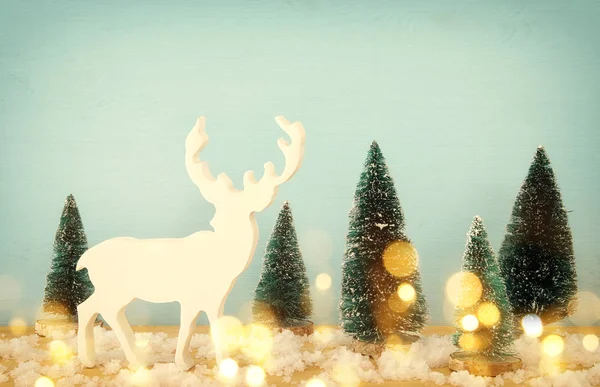 Image of christmas trees and reindeer on snowy wooden table. — Stock Photo, Image