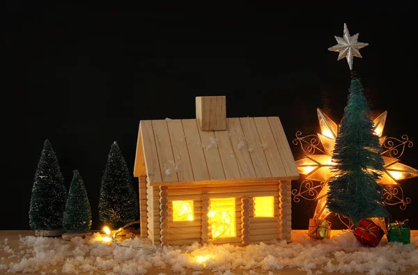 Afbeelding van de kerstboom en houten huis met licht door het raam, boven besneeuwde tafel. — Stockfoto