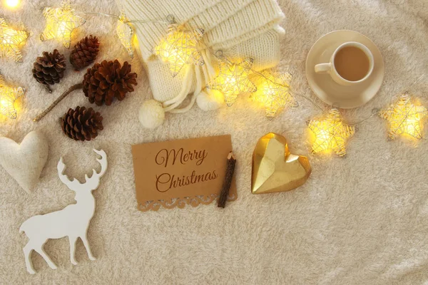 Note with text MERRY CHRISTMAS and cup of cappuccino over cozy and warm fur carpet. Top view. — Stock Photo, Image