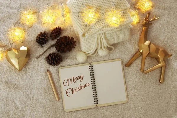 Notebook with text: MERRY CHRISTMAS and cup of cappuccino over cozy and warm fur carpet. Top view. — Stock Photo, Image