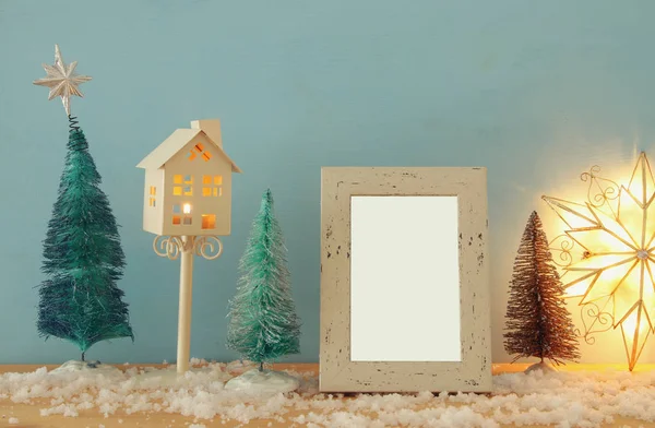 Imagen de árboles de Navidad junto a un marco de fotos vacío en una mesa de madera nevada. Para montaje fotográfico . — Foto de Stock