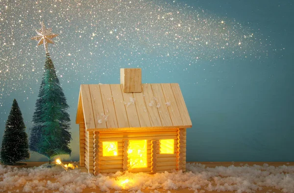 Immagine di albero di Natale e casa in legno con luce attraverso la finestra, sopra il tavolo innevato . — Foto Stock