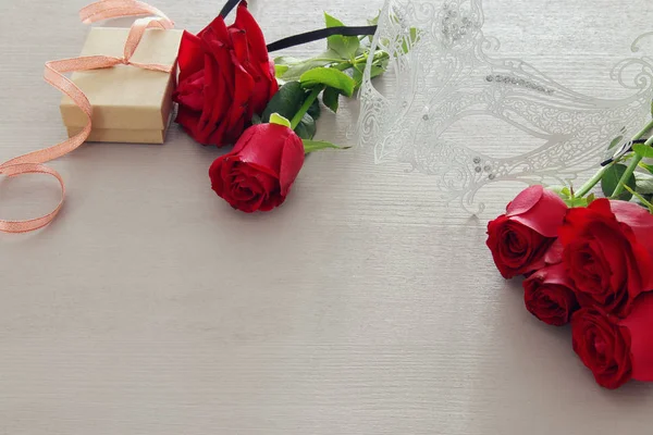 Valentijnsdag romantisch achtergrond met mooi bouquet van rozen en maskerade wit masker op houten tafel. — Stockfoto