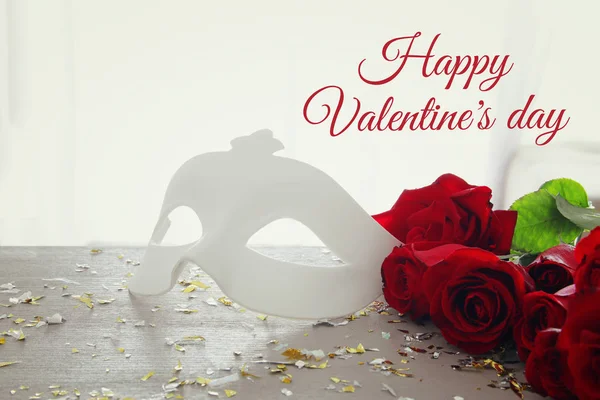 Valentijnsdag romantisch achtergrond met mooi bouquet van rozen en maskerade wit masker op houten tafel. — Stockfoto