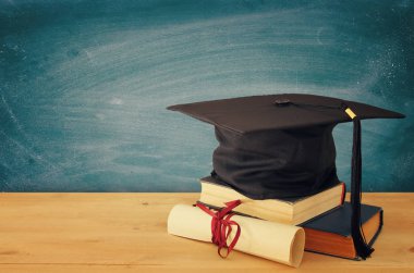 Mezuniyet siyah şapka ahşap masa üzerine mezuniyet yanındaki eski kitaplar üzerinde görüntü. Eğitim ve okul kavramı geri