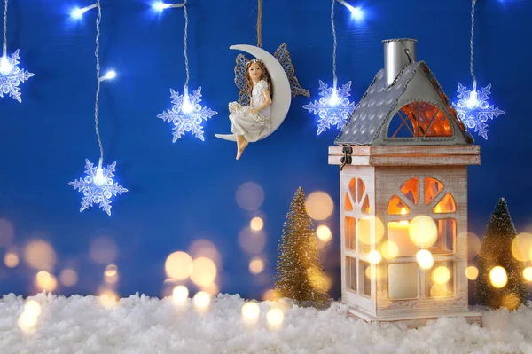 Árboles de Navidad, linterna vieja, copos de nieve luz guirnalda de plata, hada en la luna sobre la nieve y el fondo azul . — Foto de Stock