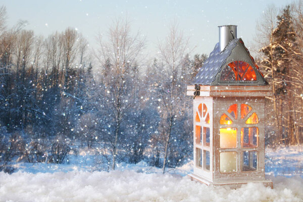 Wooden old house with candle over the snow and blurry magical winter landscape background.