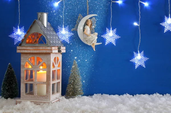 Feetjie op de maan over de sneeuw en blauwe achtergrond, kerstbomen, oude lantaarn, sneeuwvlokken zilveren garland licht. — Stockfoto