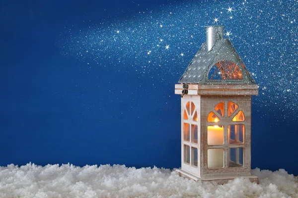 Antigua casa de madera con vela sobre la nieve y el fondo azul . — Foto de Stock