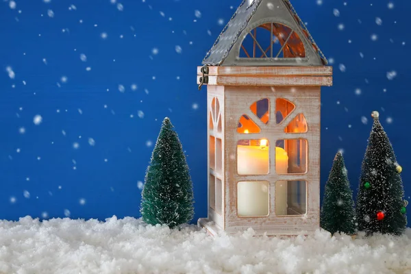 Houten oud huis met kaars naast de bomen van Kerstmis over de sneeuw en blauw nackground. — Stockfoto