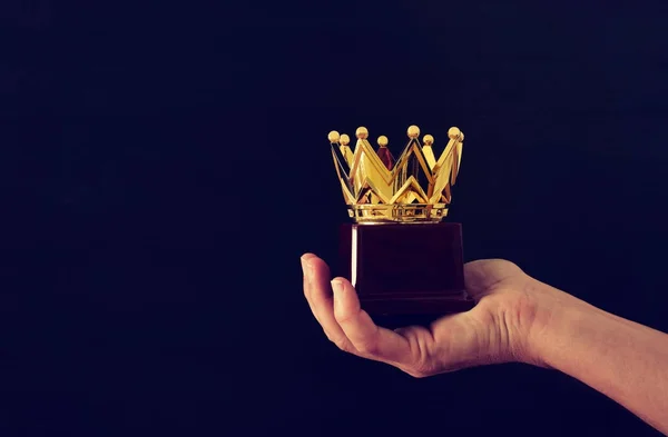 Mão do homem segurando troféu coroa prêmio para mostrar a vitória ou ganhar o primeiro lugar. Sobreposição de brilho . — Fotografia de Stock