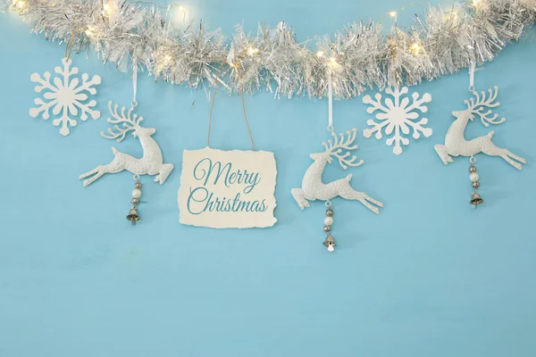 Christmas background with tree festive garland, white deer, and paper white snowflakes over light blue background. — Stock Photo, Image