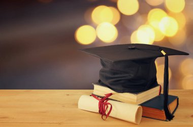 Image of graduation black hat over old books next to graduation on wooden desk. Education and back to school concept clipart